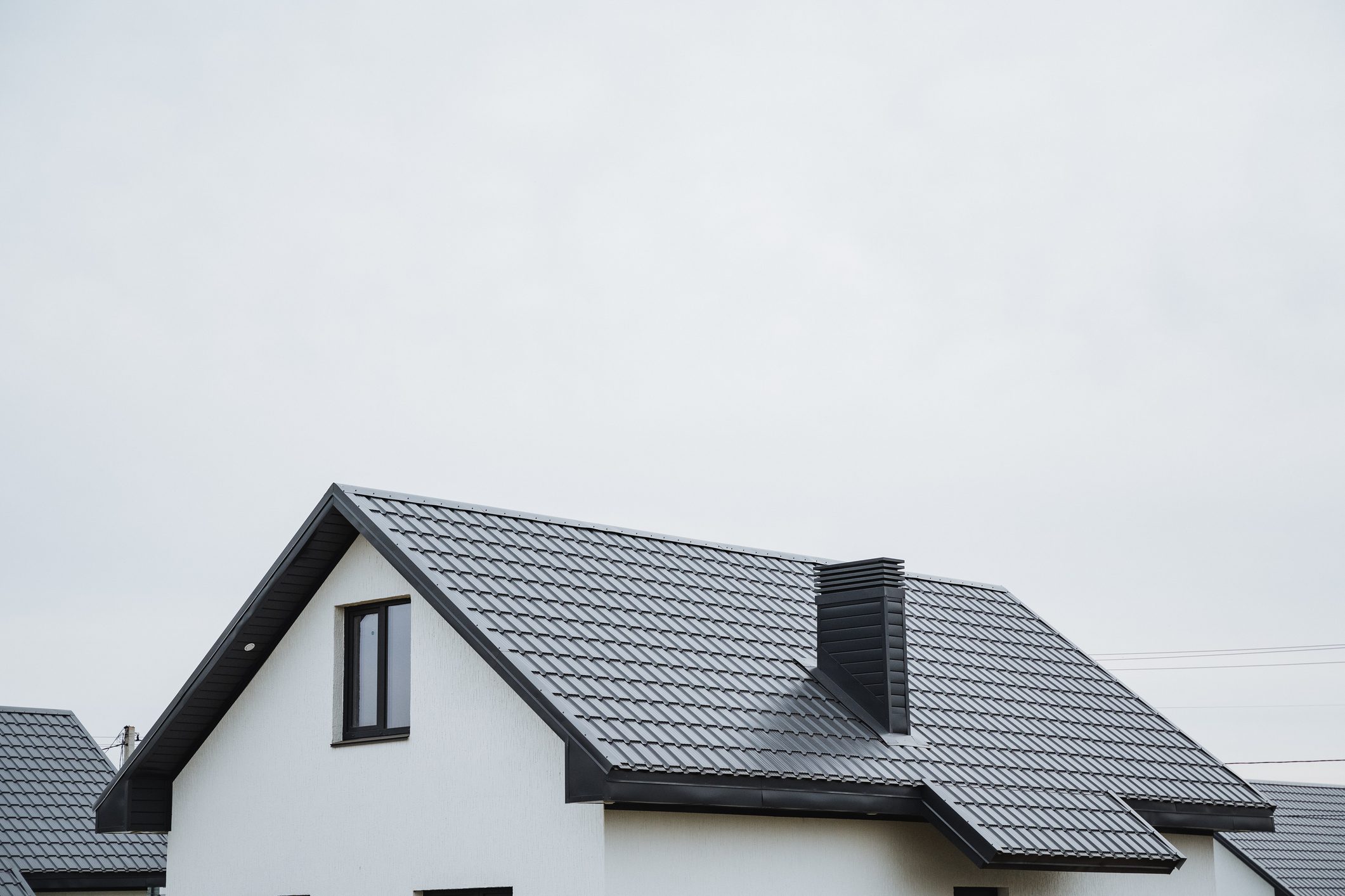 The architectural structure is a beautifully designed white house with a striking black roof and tall chimney, creating a charming and appealing appearance in its lovely surroundings